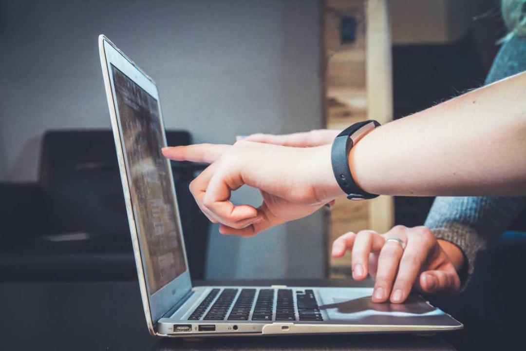 Photo of a computer and hands pointing at the screen.